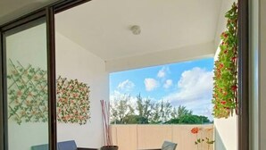En balkon med fletningsmøbler, en potteplante og udsigt til træer og himmel.