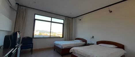 Habitación de hotel con dos camas individuales, un escritorio con silla, televisor y ventana con cortinas.