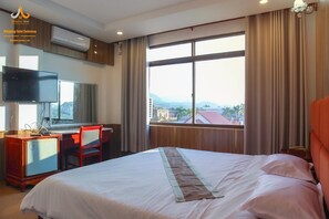Una habitación de hotel con una cama, un escritorio con silla, un televisor y un ventanal con cortinas.