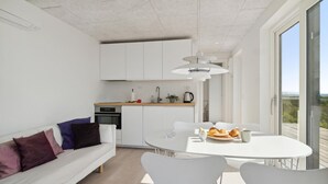 Une cuisine moderne avec des armoires blanches, un four encastré et un coin repas comprenant une table et des chaises blanches.