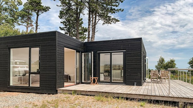Une cabane moderne aux allures  épurées, avec de grandes portes-fenêtres coulissantes, une terrasse en bois et une cuisine ouverte.