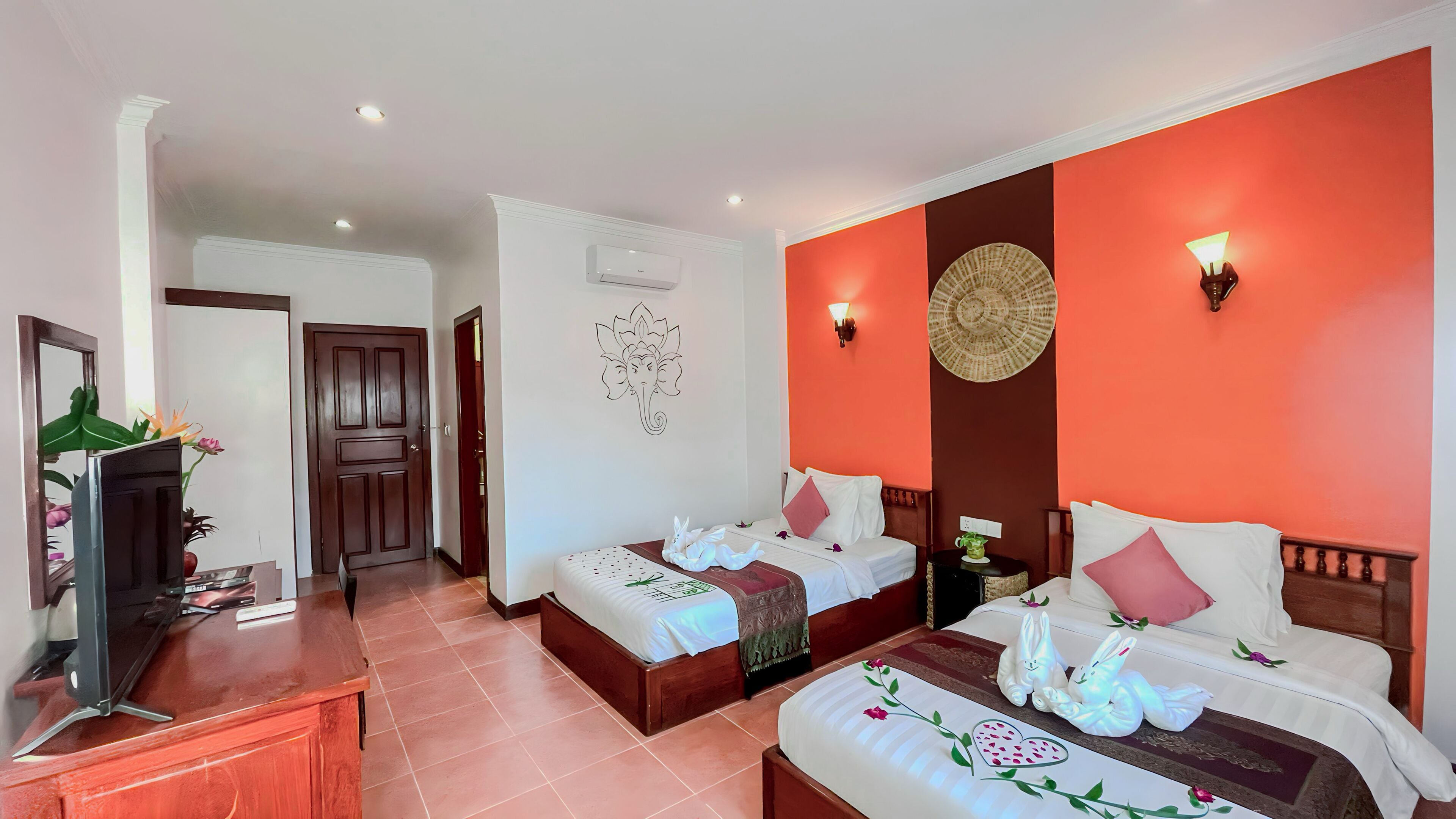 A hotel room with two beds, a desk, a mirror, and a wall with a decorative wall hanging.