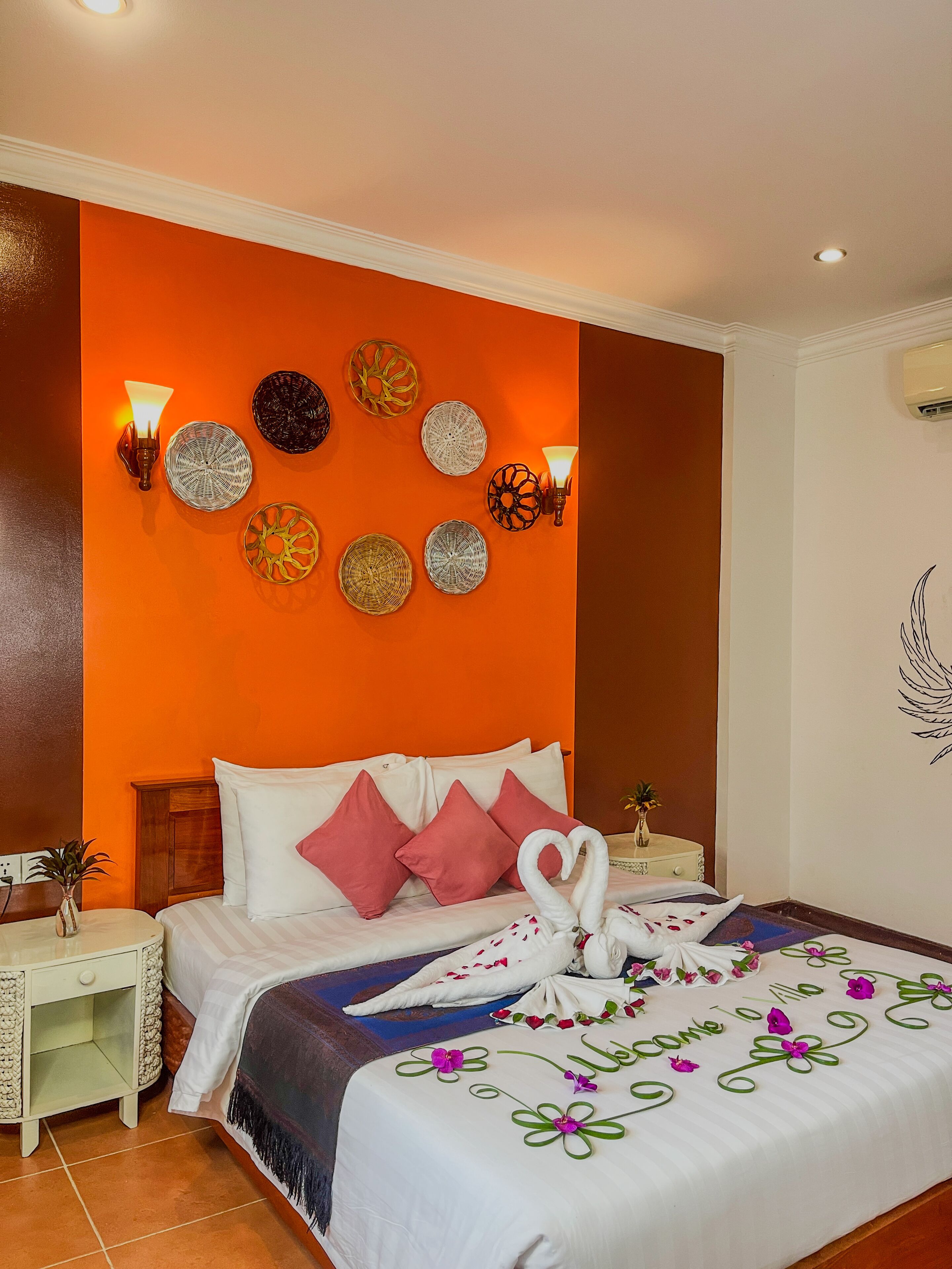 Habitación de hotel con cama, almohadas, mesita de noche, lámpara de pared, platos decorativos y una obra de arte en la pared.