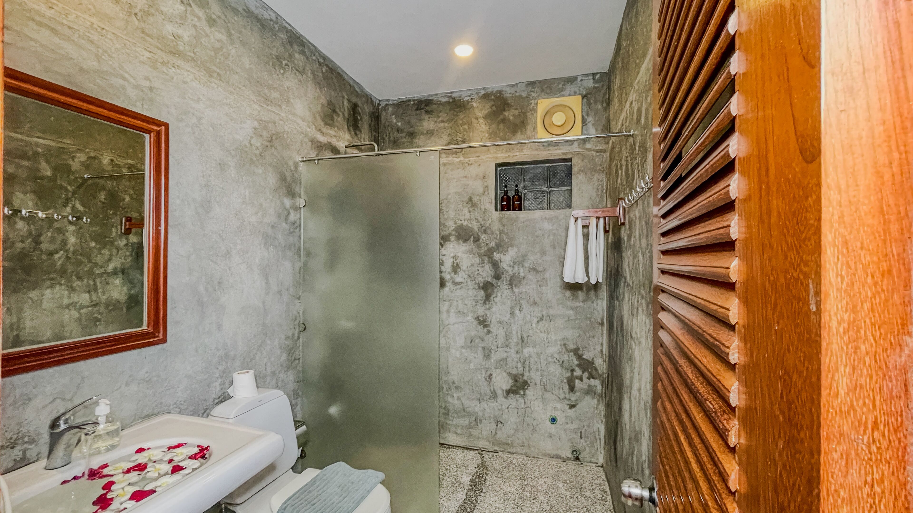 Ein Badezimmer mit Dusche, einem Spiegel, einem Waschbecken mit Seife und Handtüchern an einem Haken.