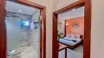A hotel room with a bed, a mirror, a wall-mounted light fixture, and a view of the bathroom.