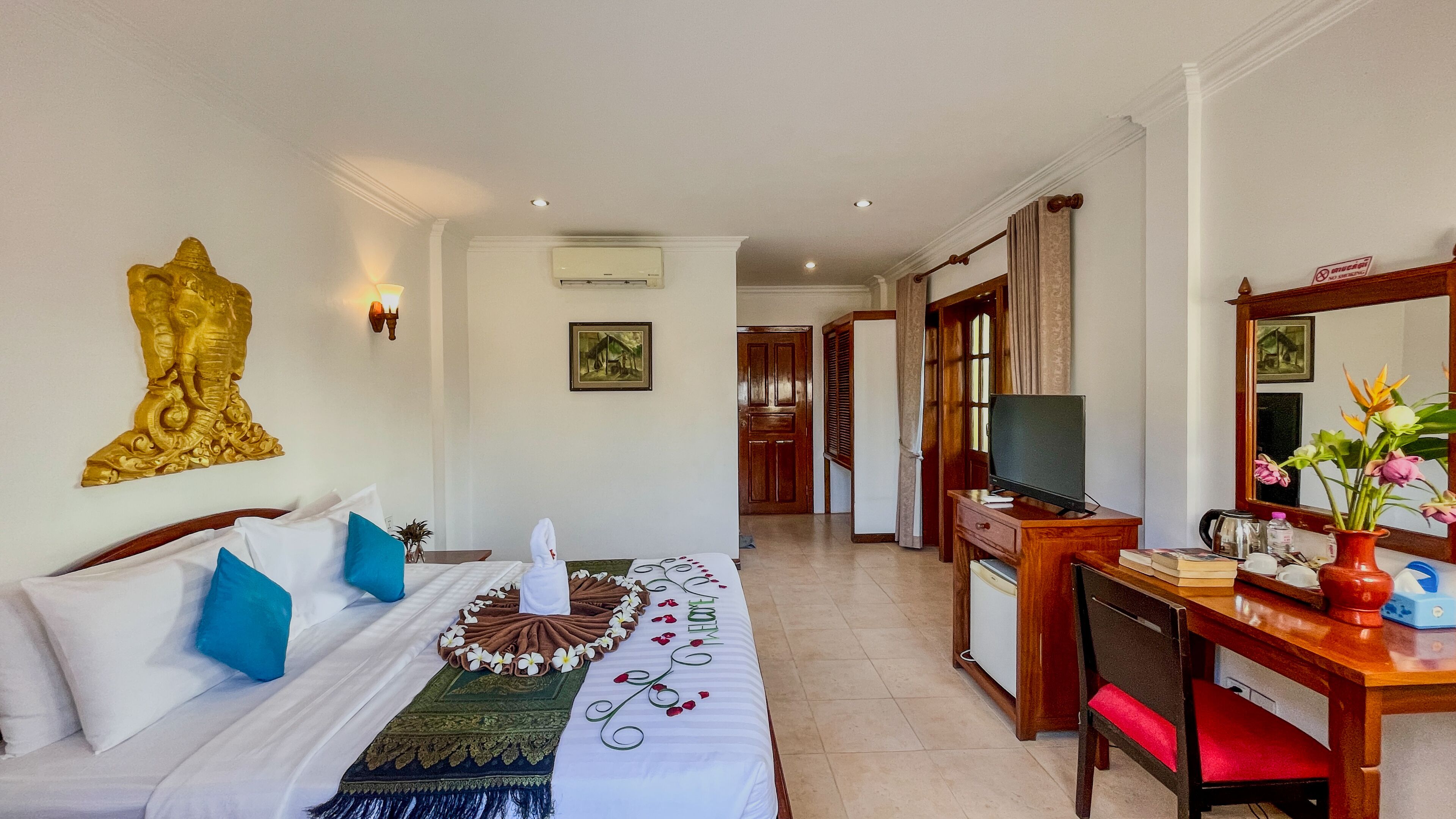 A hotel room with a bed, a desk with a TV, a mirror, and a wall-mounted air conditioner.