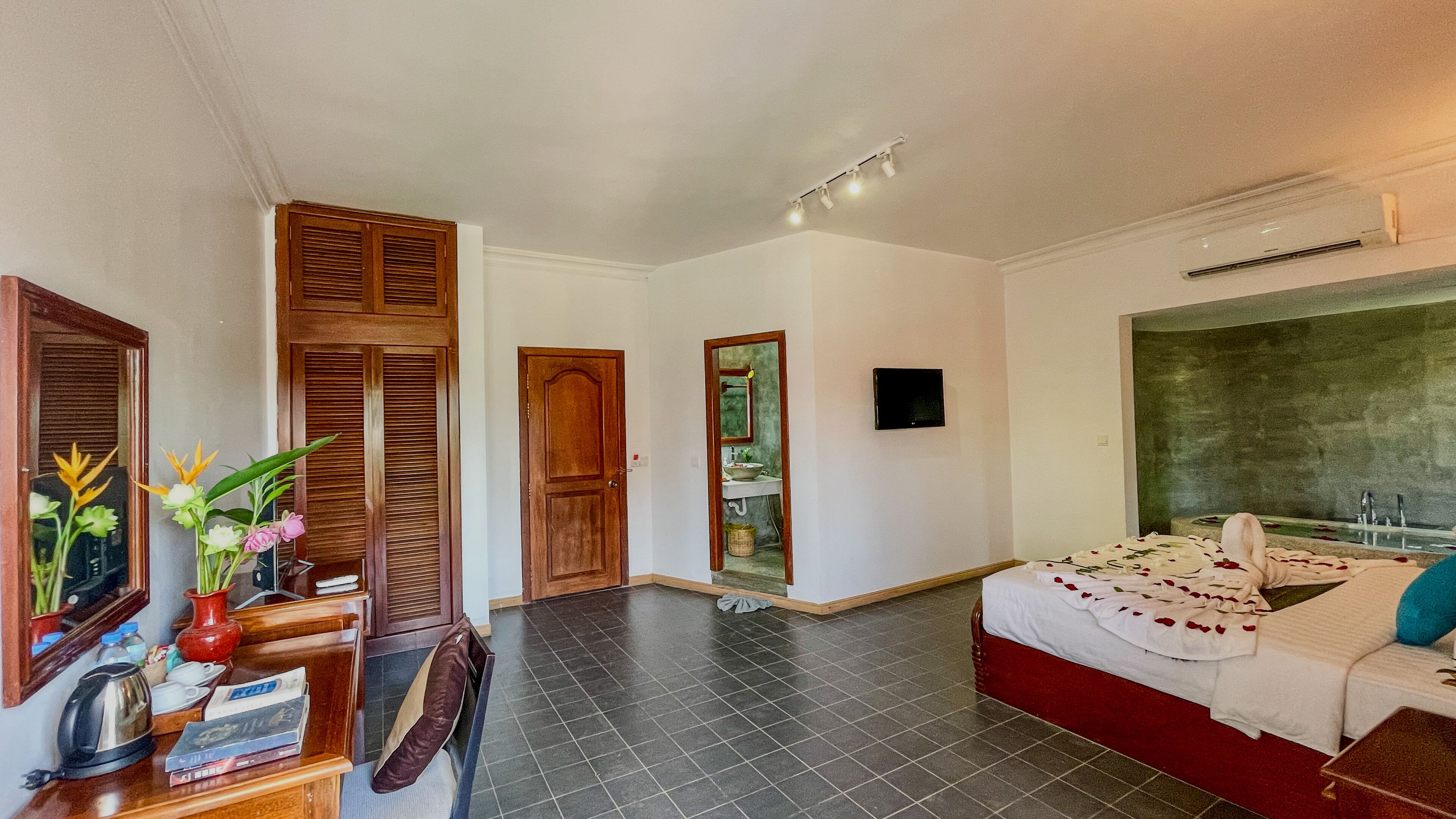A hotel room with a bed, a desk with a chair, a TV, and a bathroom visible through an open door.