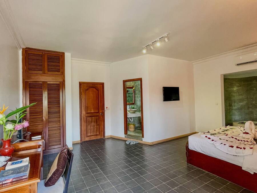 A hotel room with a bed, a desk with a chair, a TV, and a bathroom visible through an open door.