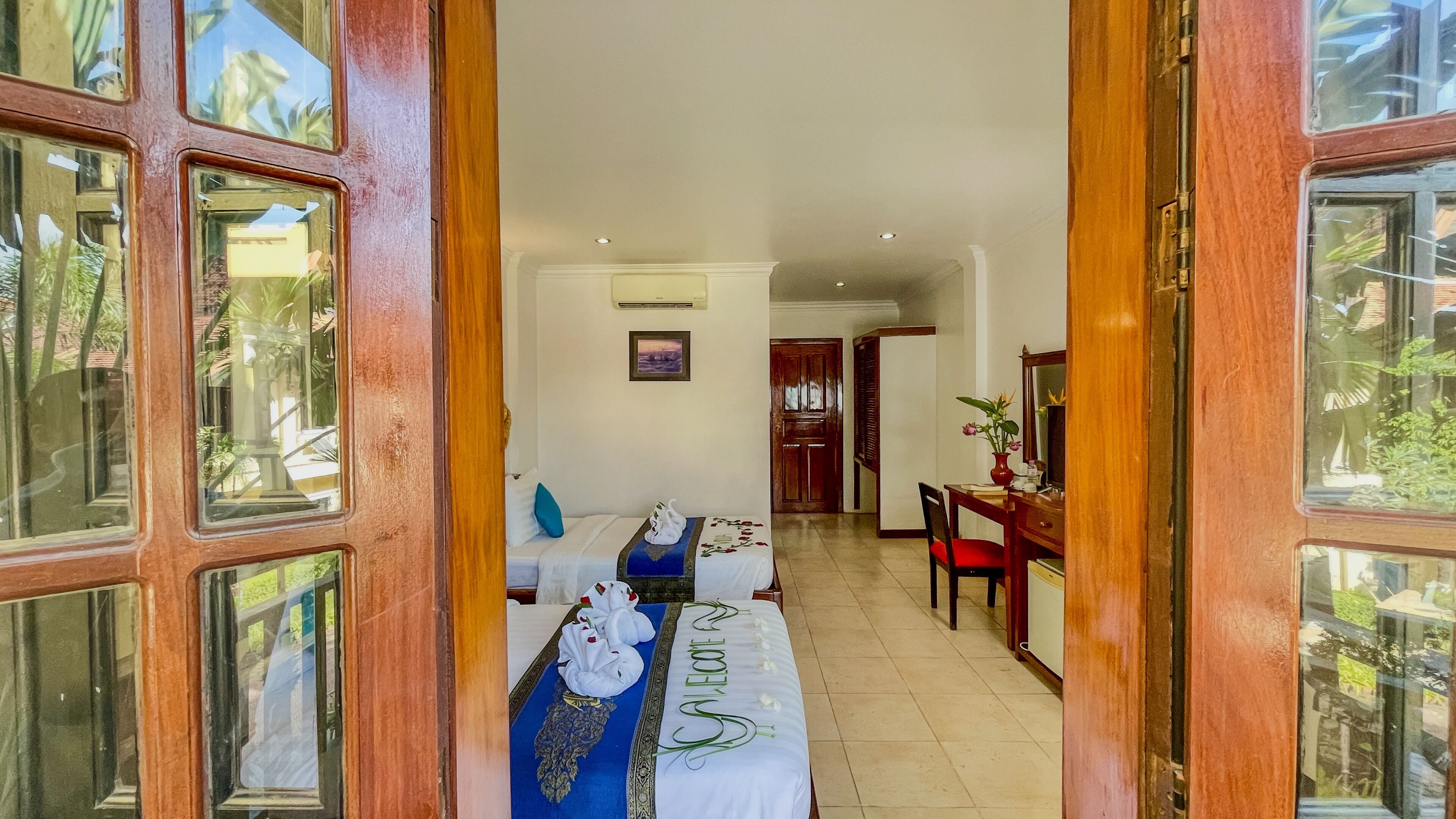 Quarto de hotel com cama, escrivaninha e uma cadeira. Uma porta dá acesso a outro cômodo.