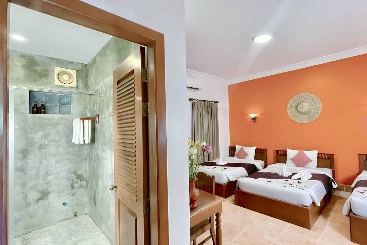 A hotel room with a shower area, two beds, a table, and a vase with flowers.