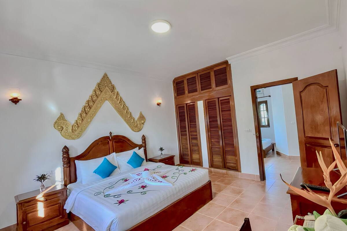 A bedroom with a wooden bed, a nightstand, a wall-mounted light, and a large mirror.