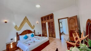 A bedroom with a wooden bed, a nightstand, a wall-mounted light, and a large mirror. - Villa Indochine d'Angkor (Siem Reap)