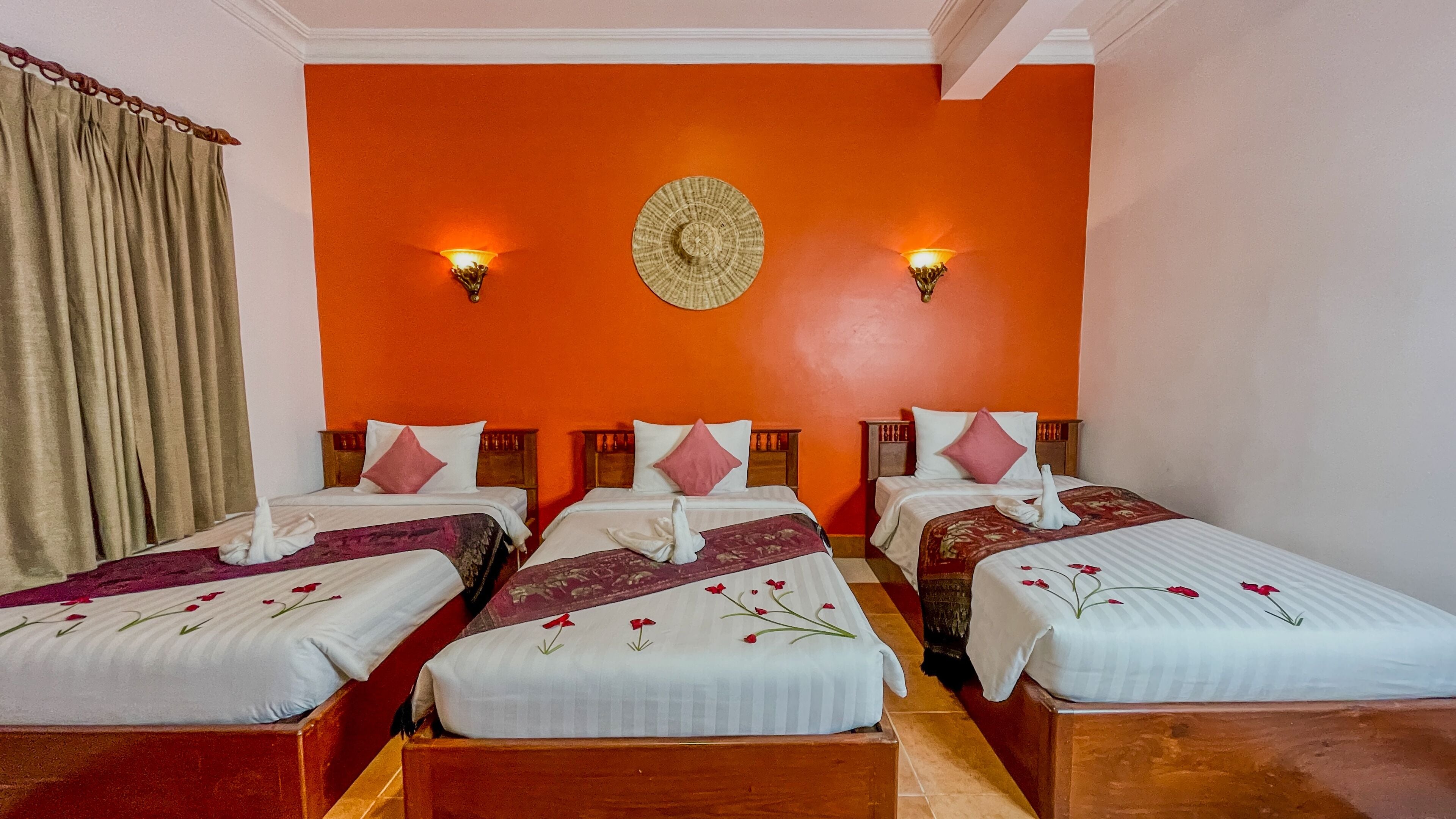 A hotel room with three beds, orange walls, and two wall-mounted lamps.