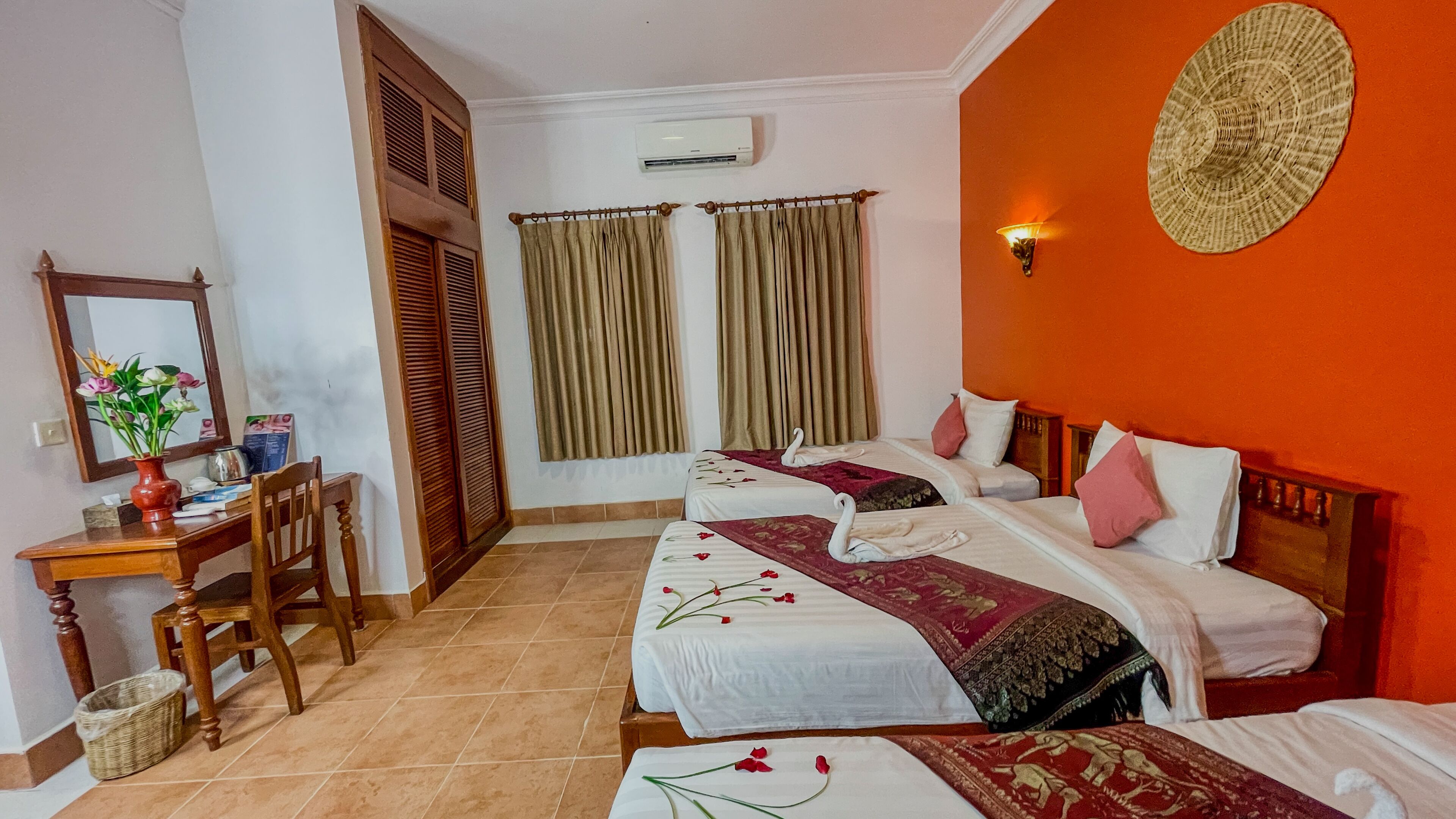Une chambre d’hôtel avec deux lits, un bureau, une chaise, un miroir et un climatiseur fixé au mur.