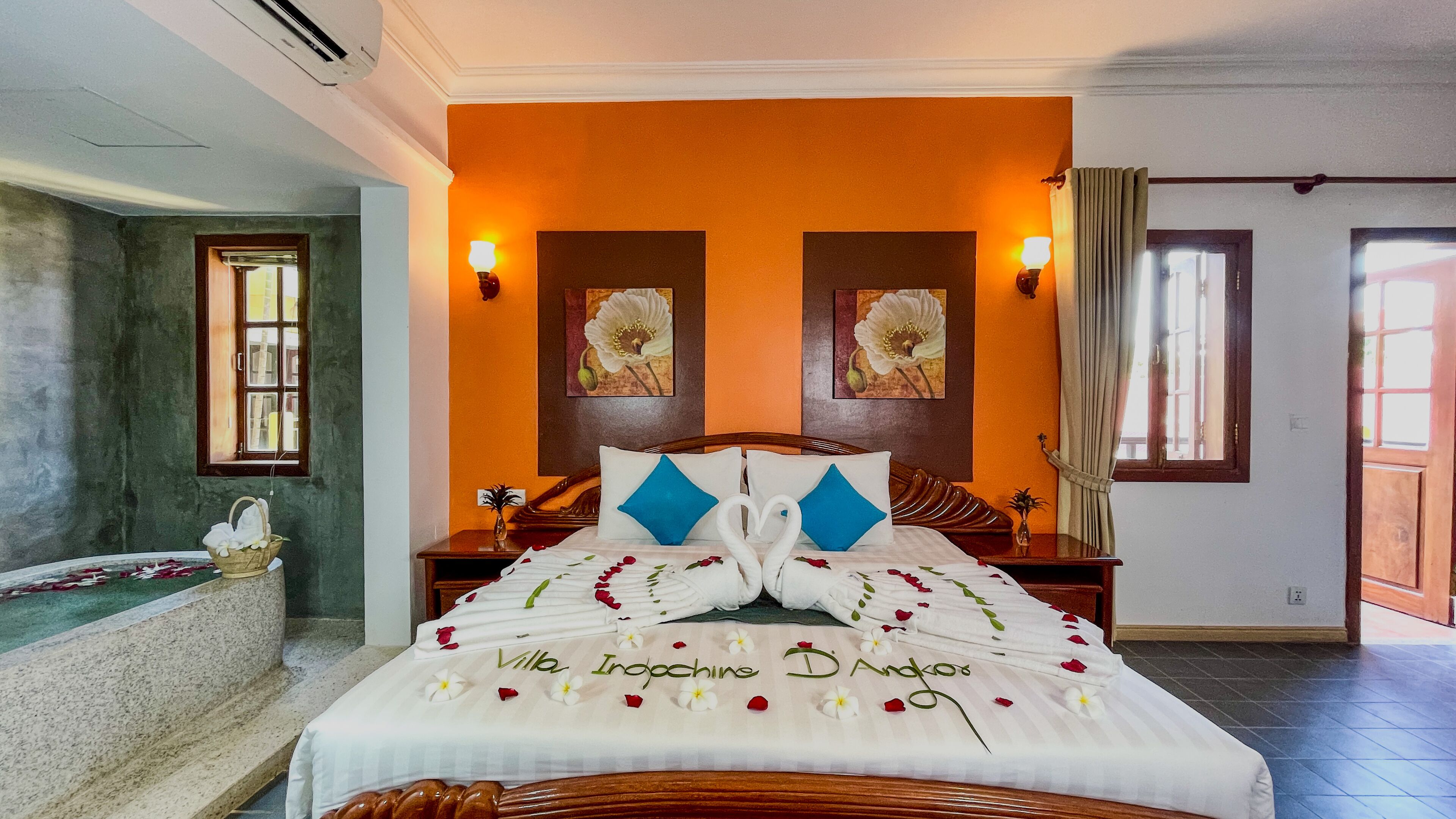 A hotel room with an orange accent wall, a bed with a floral bedspread, a bathtub, and two wall-mounted lamps.