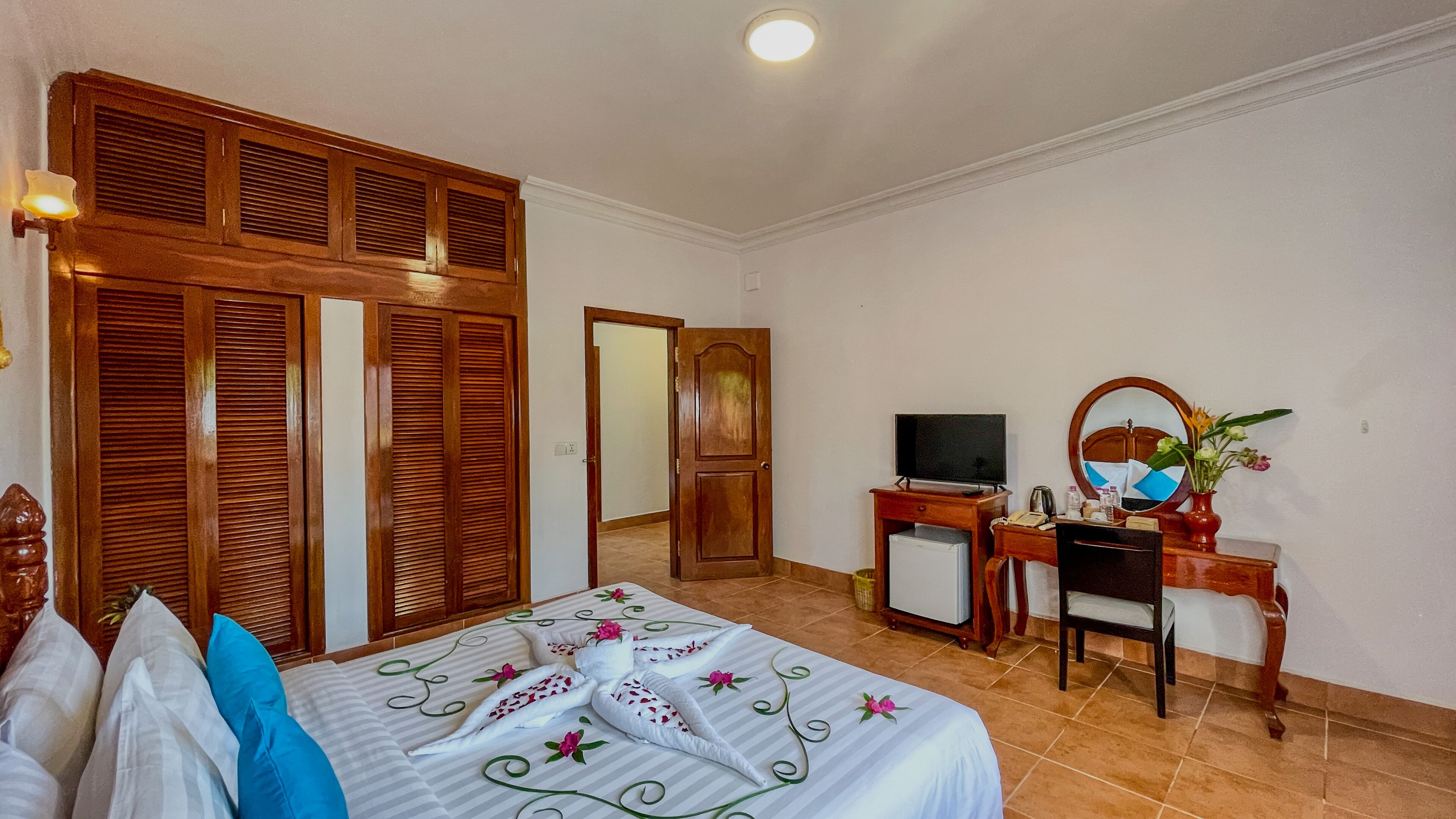 Une chambre d’hôtel comprenant un lit, un bureau avec une télévision, un petit réfrigérateur, un miroir et une armoire en bois.