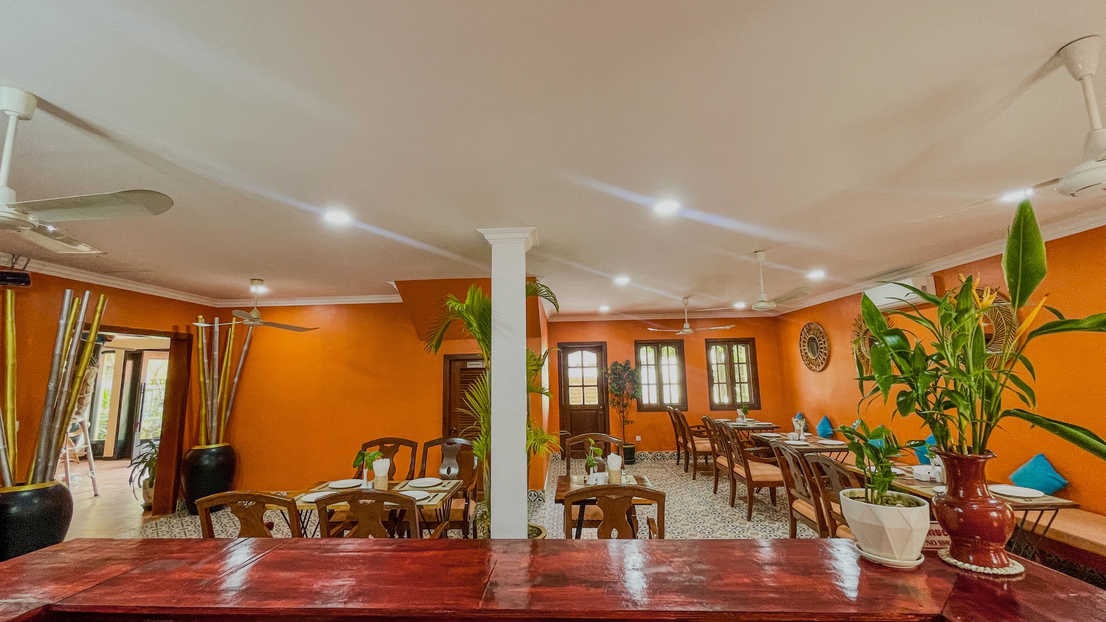 A dining area with multiple tables and chairs, ceiling fans, and potted plants.