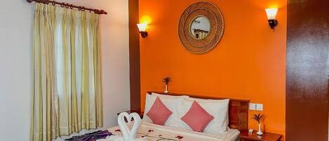 A hotel room with an orange wall, a bed with white and pink pillows, a decorative mirror, and two wall-mounted lights.