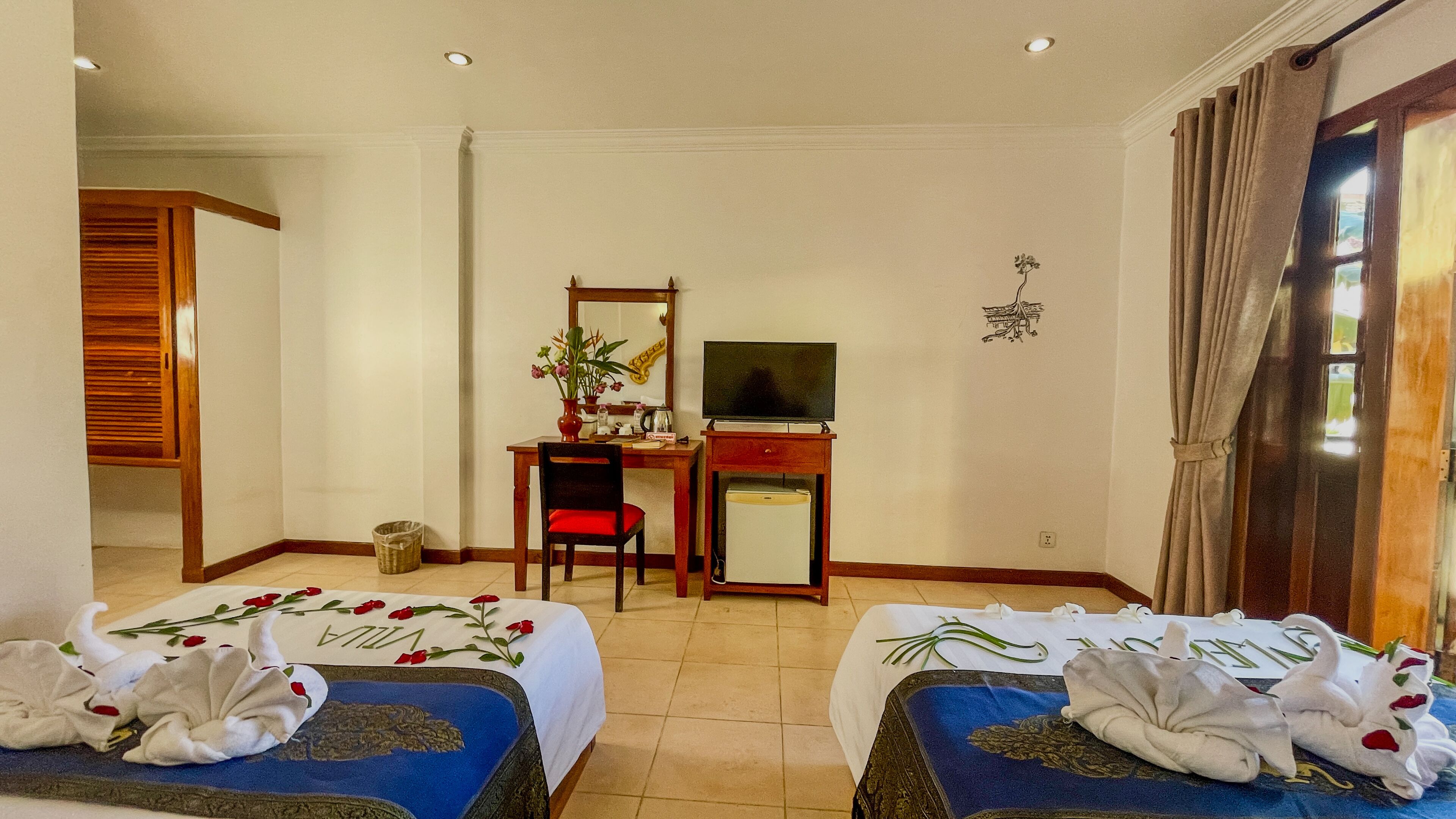 Quarto de hotel com duas camas, uma escrivaninha com televisão, uma cadeira e um pequeno frigorífico.