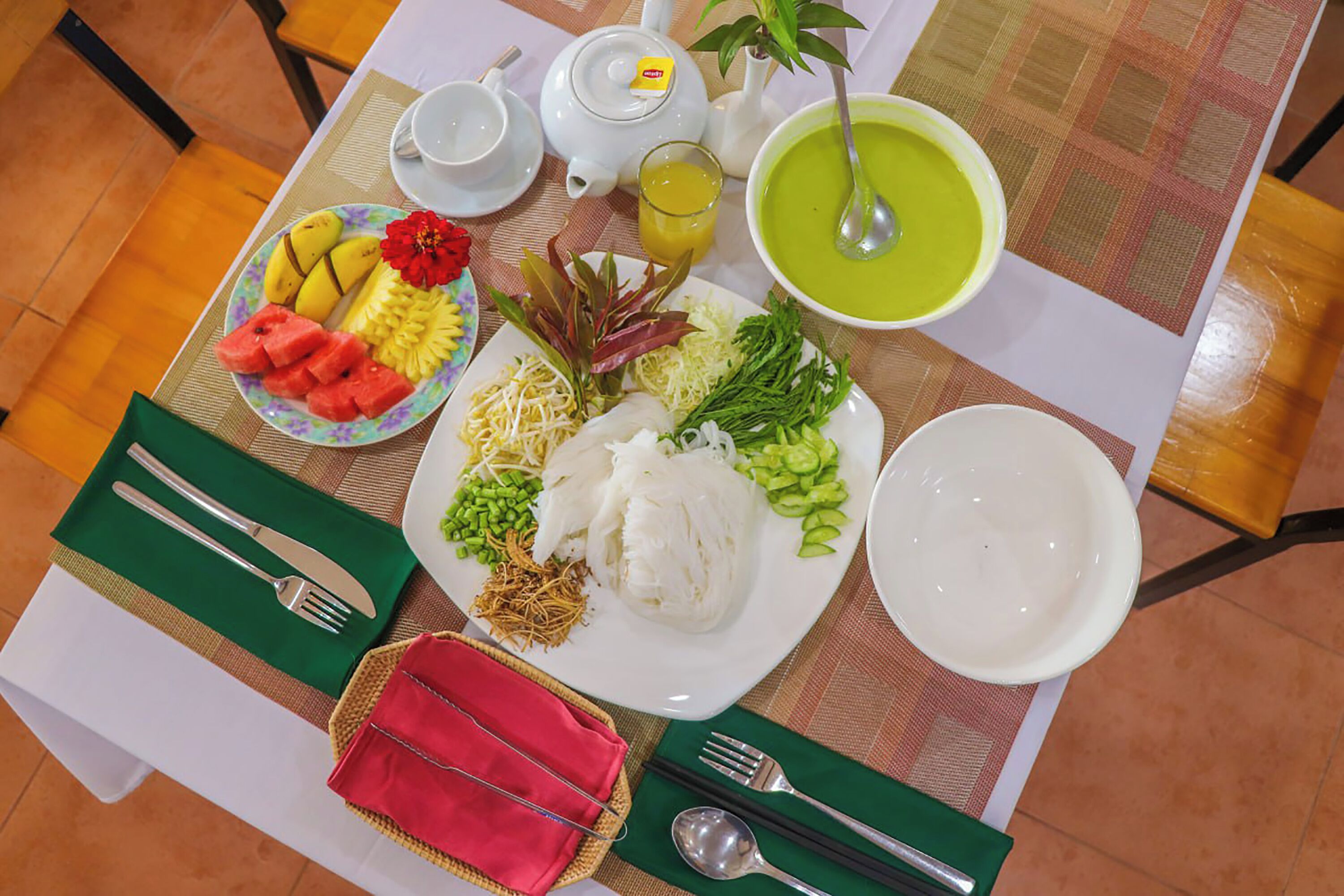 A table set with a variety of dishes including a bowl of soup, a plate of vegetables, and a plate of fruit.