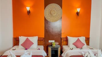 A hotel room with two beds, each with white linens and pink pillows, a small round side table with a woven basket, and two wall-mounted lamps.