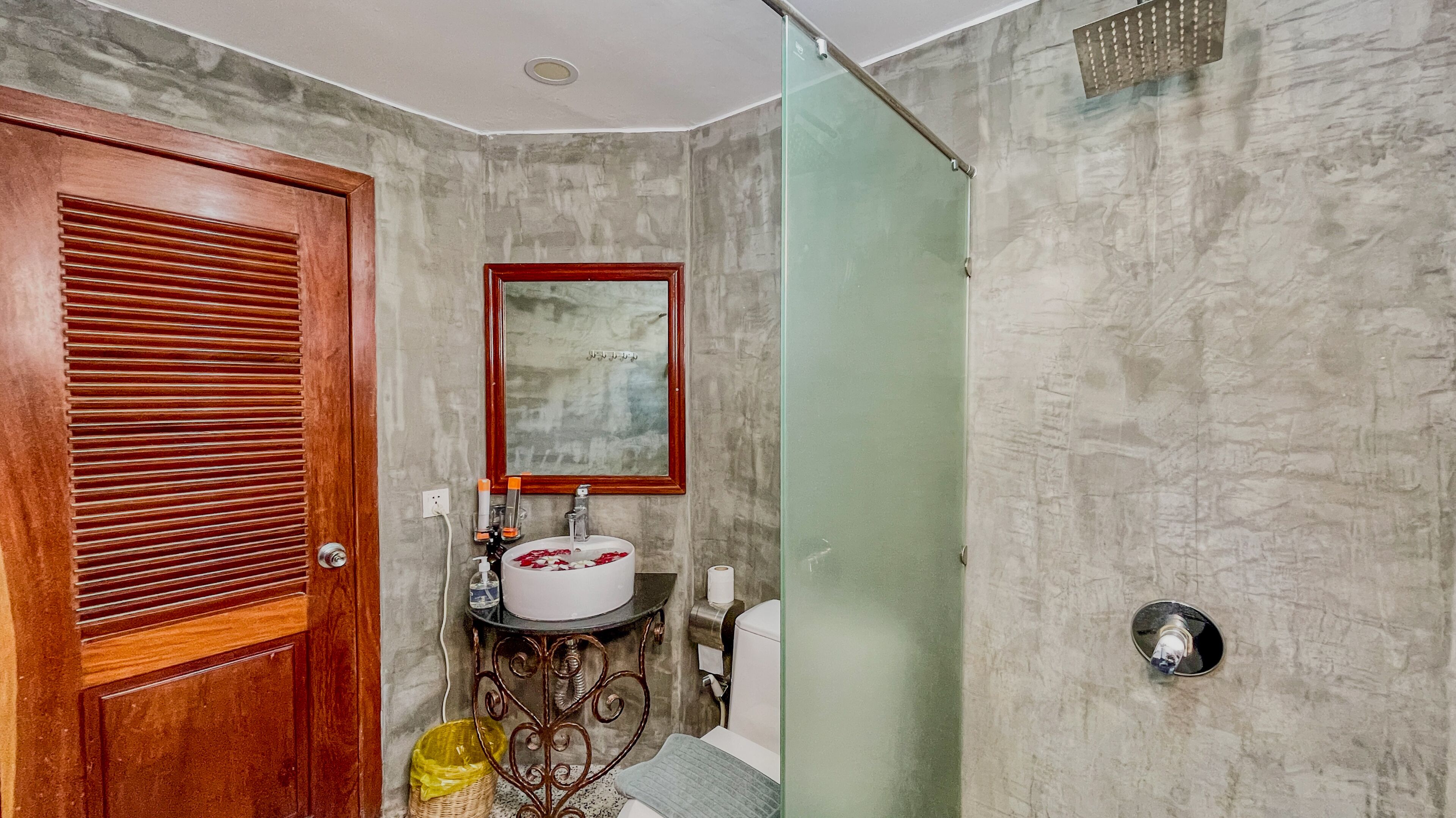 Ein Badezimmer mit Holztür, Waschbecken mit Spiegel, Dusche und Toilette.