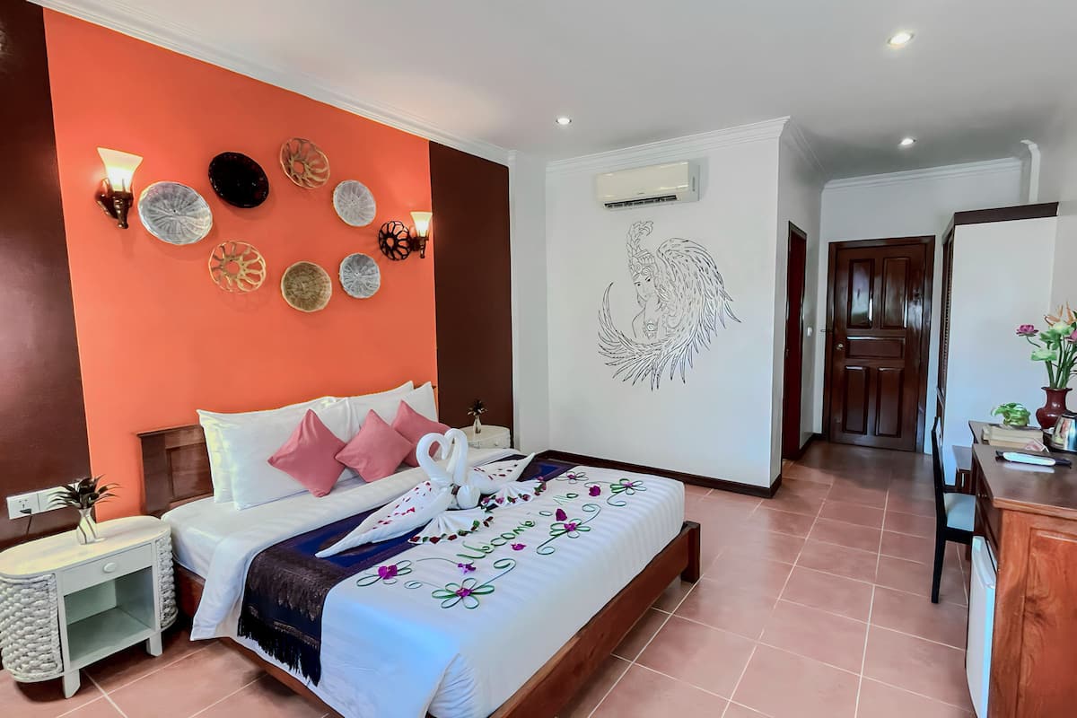 A hotel room with a bed, a nightstand, a dresser, a TV, and a wall with decorative plates and a wall decal.