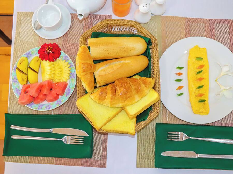A breakfast setting with croissants, bread, an omelette, and fruit on plates, along with cutlery and a teapot.