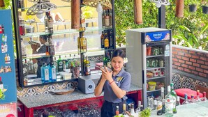 Zona de bar con una variedad de botellas de licor, vasos y un refrigerador lleno de bebidas.