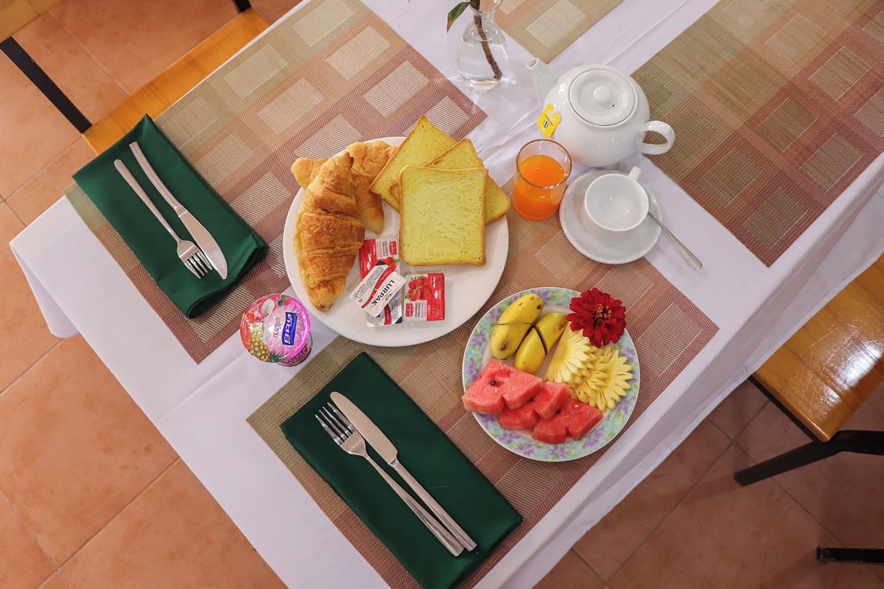 Une table de petit-déjeuner avec des croissants, des toasts, des fruits et une théière.