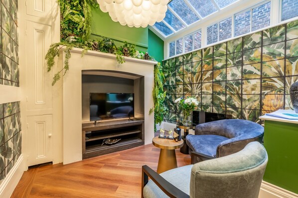 A cozy living room with a fireplace, comfortable seating, and a green accent wall with a tropical mural.