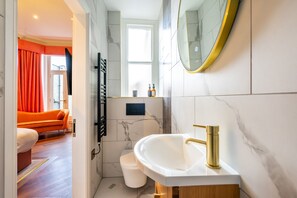Ein modernes Badezimmer mit einem weißen Waschbecken, einem goldfarbenen Wasserhahn und einem großen Spiegel.