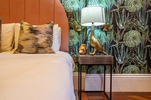 Ein Schlafzimmer mit einem Bett, Kissen, einem Nachttisch mit Lampe und einer Wand mit Blumenmuster-Tapete.