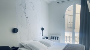 Een moderne slaapkamer met een marmeren wand, een bed met witte lakens, een donkere hoofdbord en uitzicht op een balkon.