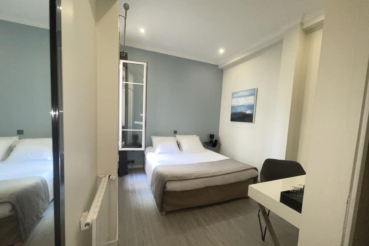 Habitación de hotel con dos camas, un escritorio, una silla, un cuadro en la pared y una ventana con vistas.