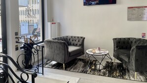 Een moderne woonkamer met twee grijze fauteuils, een klein rond bijzettafeltje en een groot raam met uitzicht op de stad.
