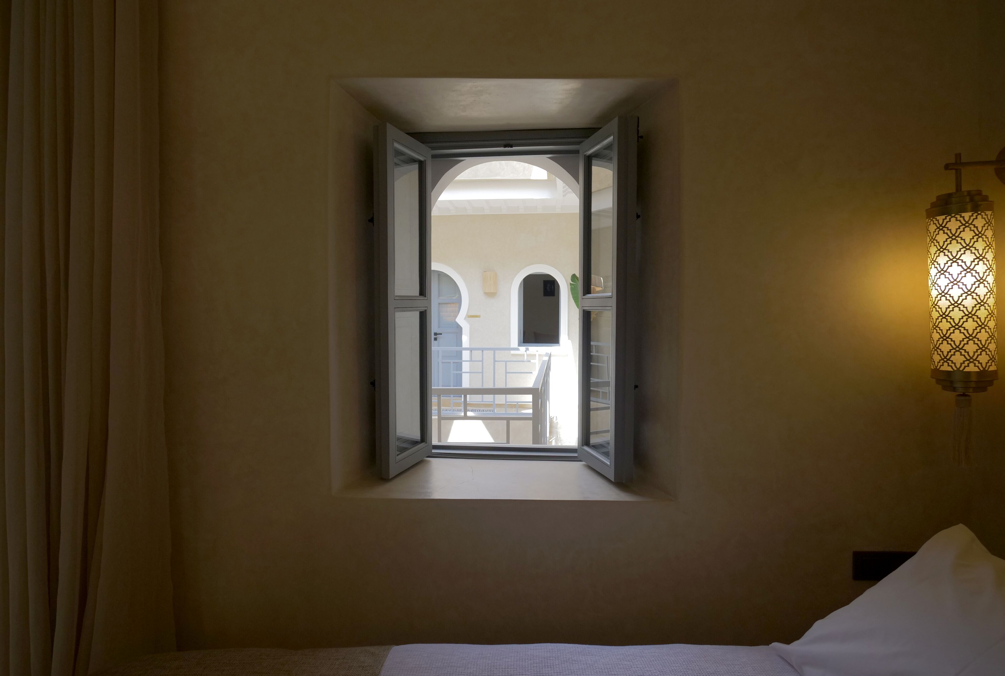 Un dormitorio con ventana, cama y lámpara fijada a la pared.