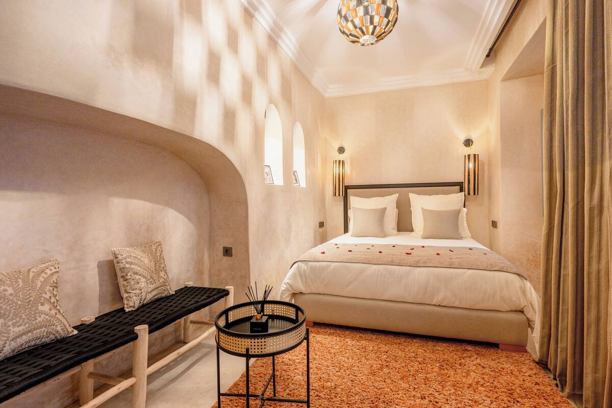 A bedroom with a bed, a bench, a small table with a candle holder, and a unique ceiling light fixture.