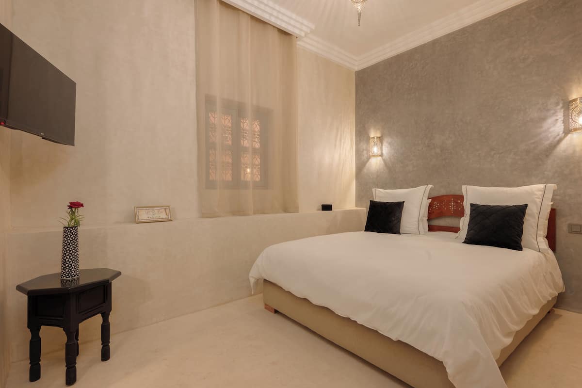 A bedroom with a bed, a small table with a vase, and a wall-mounted TV.