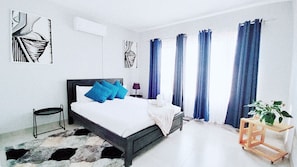 A bedroom with a bed, a nightstand, a lamp, a plant, and a window with curtains. - MillsPad  (Mbombela)