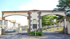 Une entrée fermée par un portail, surmontée d’une arche en pierre, avec une boîte aux lettres et une allée pavée menant à un bâtiment.