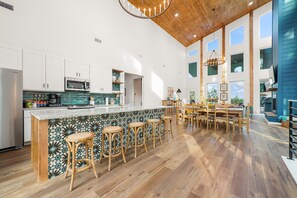 Une cuisine spacieuse dotée d’un grand îlot central, de tabourets de bar en bois et d’un coin repas avec une table et des chaises en bois.