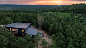 Ett modernt hus omgivet av tät skog med en fri utsikt över solnedgången.