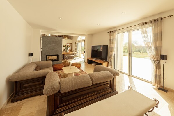 A modern living room with a sectional sofa, a flat-screen TV, and a dining area with a table and chairs. - Aux Truffes de Combecave (Mauroux)