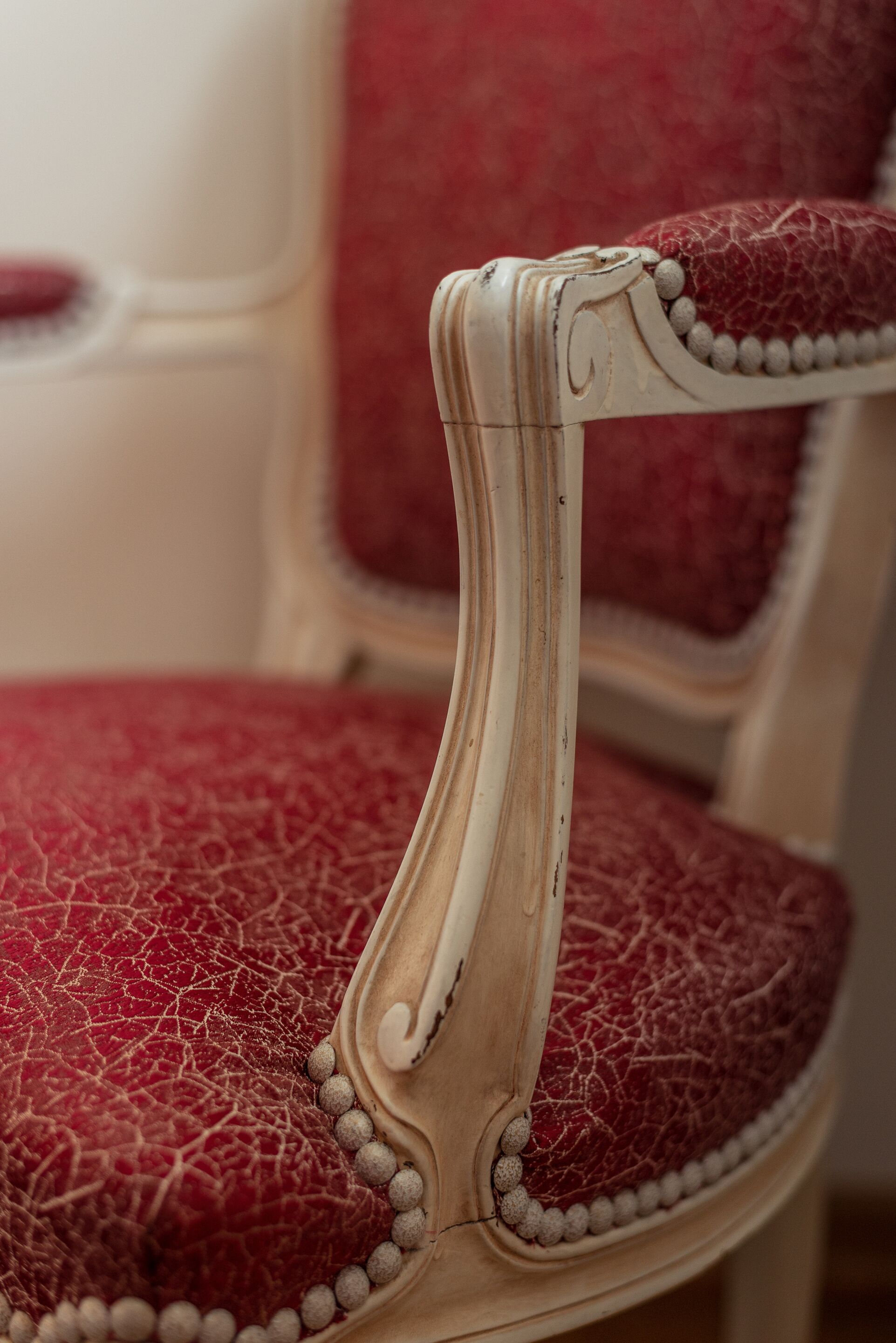 Een detailopname van een klassieke stoel met een rode leren zitting en een crème kleurig houten frame met decoratieve details.