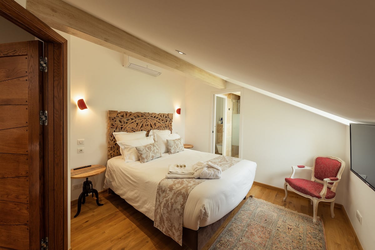 A bedroom with a large bed, a wooden headboard, a red chair, and a television on the wall.