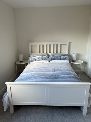 A white bed with a headboard, two bedside tables, and a grey carpeted floor.