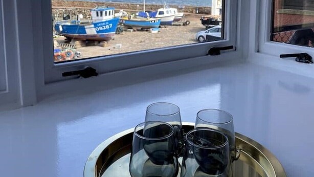 A window with a view of boats at a dock, a tray with glasses, and a white wall.