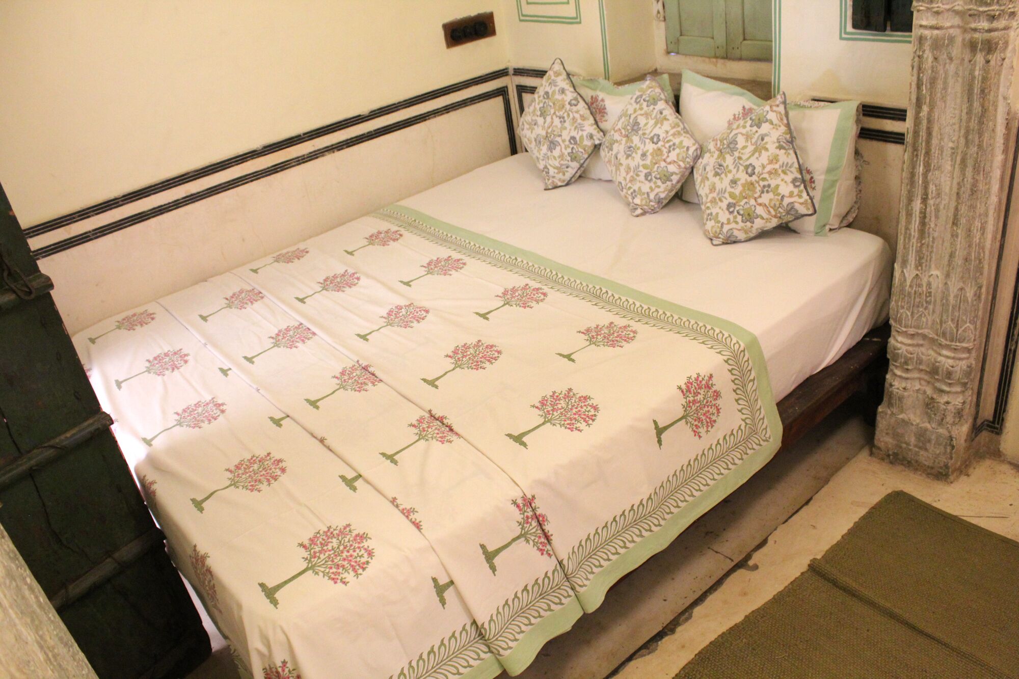 A bed with a floral-patterned bedspread, pillows with a floral design, and a green border.