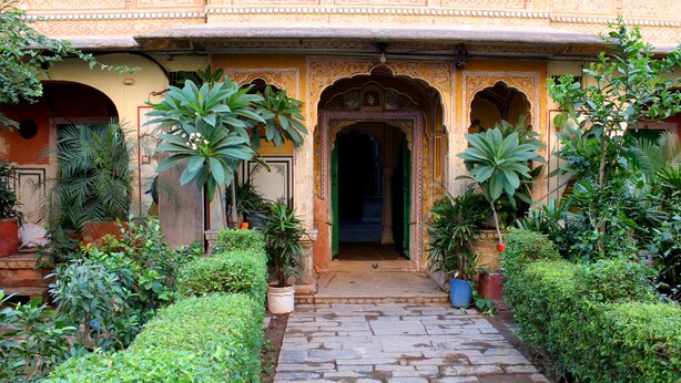 Um edifício tradicional com arquitetura detalhada, um caminho de pedra e vegetação exuberante.